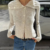 Person wearing a beige knitted cardigan and blue jeans standing on a street.